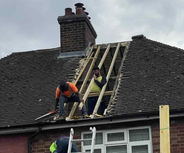 This is a photo of a roof repair being carried out. A section of the roof has been stripped and two roofers are replacing the rafters. Works being carried out by KJ Roofing Crofton